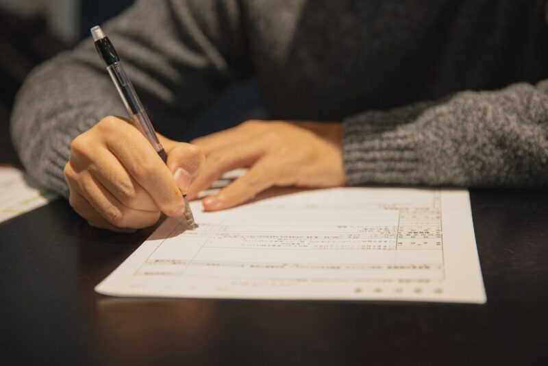 Man's hands and arms, filling in a paper form with a pen