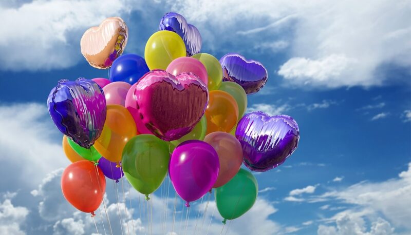 multi-colored balloons floating in a blue sky with white clouds