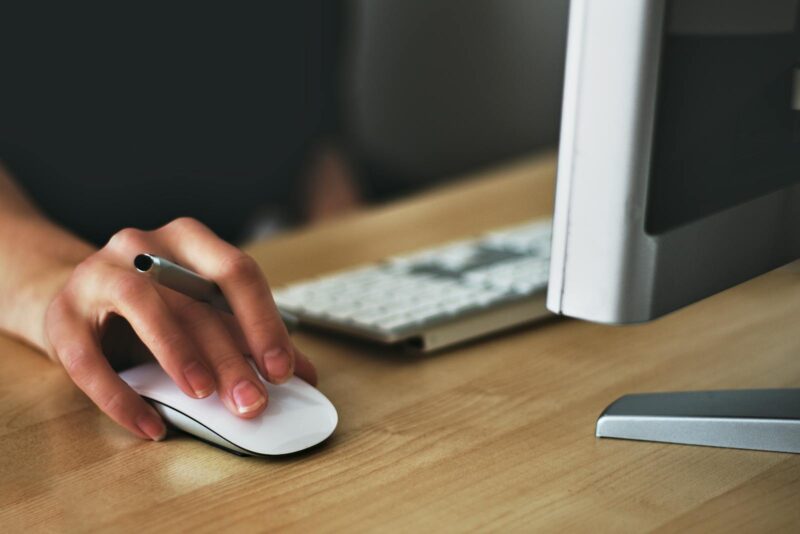 Hand of person using computer mouse with portion of keyboard and screen visible also