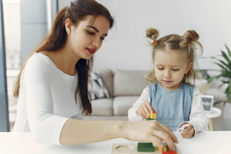 Young woman playing with a girl in denim dress